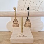 Deux porte-clés en bois bonnet de la marque Les Petites Hirondelles avec un lien vert et un lien doré sur un présentoir en bois