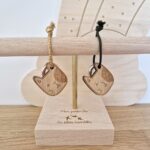 Deux porte-clés en bois chat de la marque Les Petites Hirondelles avec un lien vert et un lien doré sur un présentoir en bois