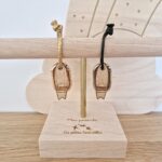 Deux porte-clés en bois surf de la marque Les Petites Hirondelles avec un lien vert et un lien doré sur un présentoir en bois